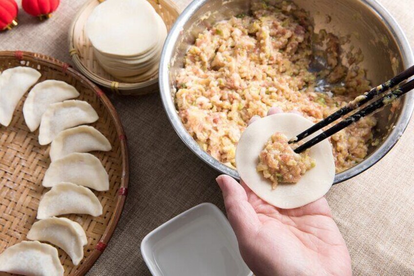 A hand holding a dumpling with chopsticks, a bowl of filling, and a basket of dumplings. 5