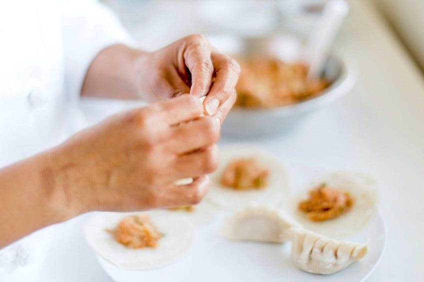 Hænder forbereder dumplings på en hvid tallerken. 1