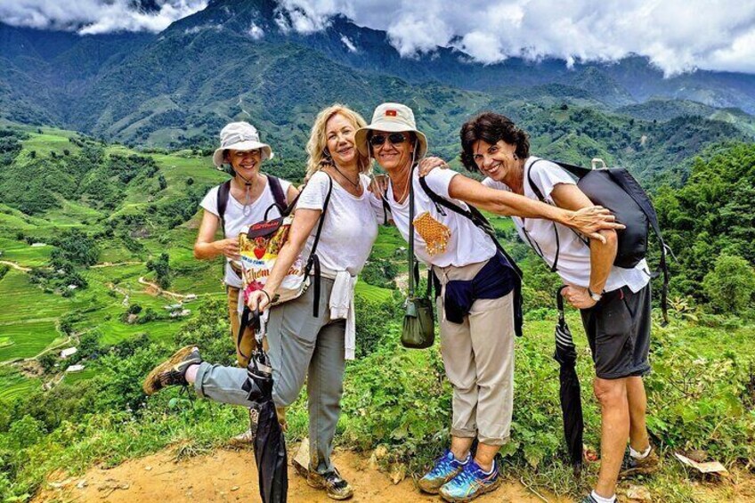 Four people hiking on a mountain trail with lush greenery and mountains in the background. 5
