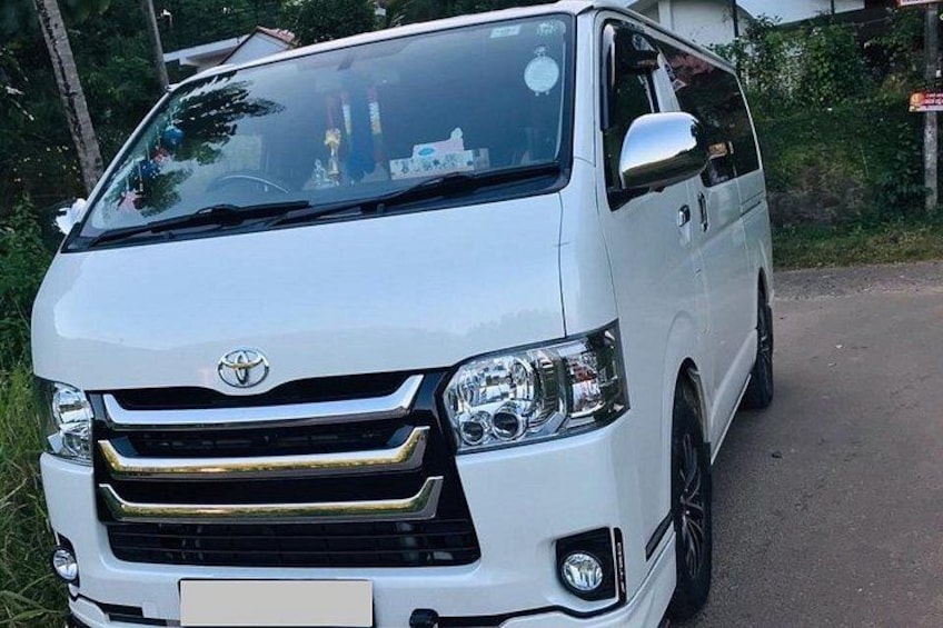 En vit Toyota-skåpbil parkerad på en asfalterad väg, med grönska i bakgrunden. 2