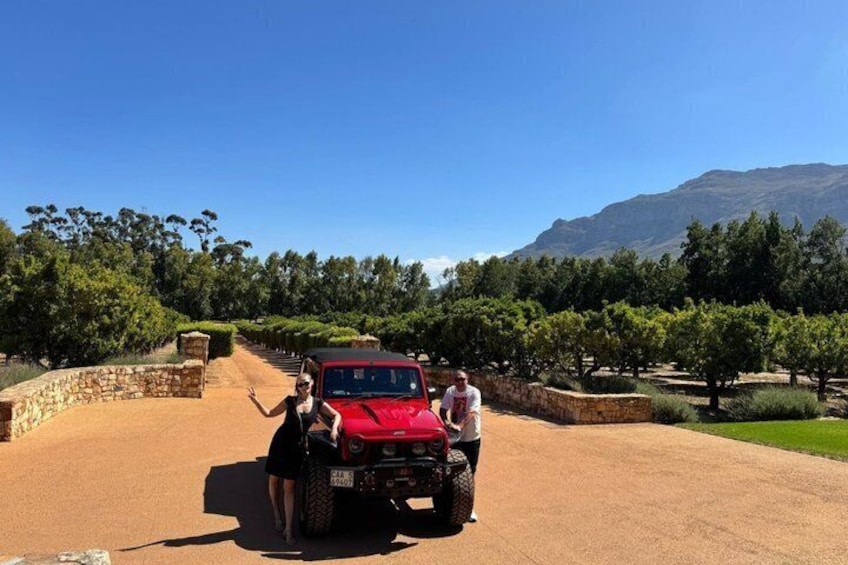 Un vehículo todoterreno rojo sobre un camino de tierra, con un muro de piedra y árboles al fondo. 4
