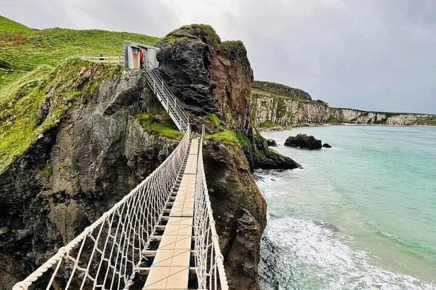 A suspension bridge over a coastal cliff, a rocky shoreline, and a small building on the cliff. 5