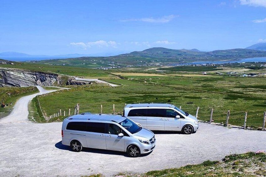 Two white vans parked on a gravel road with a scenic view of green fields and mountains in the background. 3