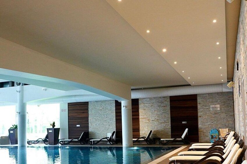 An indoor swimming pool with lounge chairs and a stone wall. 3