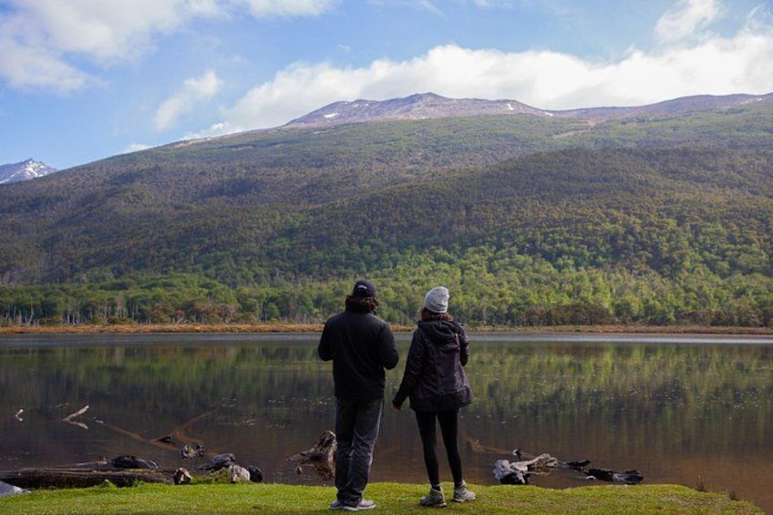 Dos personas de pie junto a un lago, con una montaña al fondo. 1