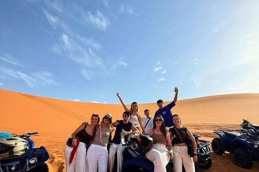 Eine Gruppe von Menschen in einer Wüstenlandschaft mit Sanddünen und Geländefahrzeugen. 5