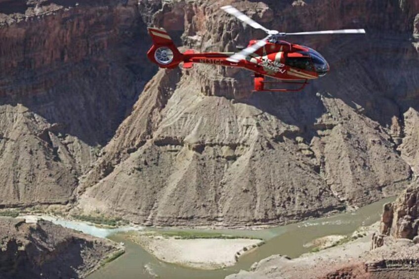 A red helicopter flying over a canyon with a river below. 2