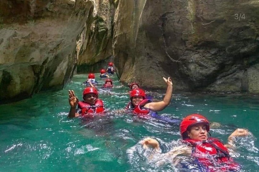 People in red helmets and life vests swimming in a narrow, rocky waterway. 4