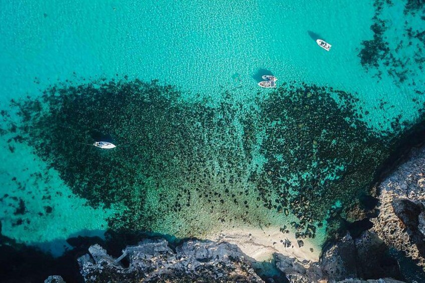 A turquoise sea with boats, a sandy beach, and rocky outcrops. 4