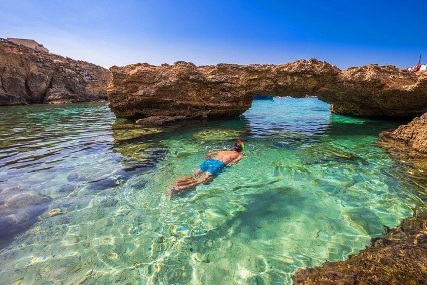 A person snorkeling in clear water with rocky formations and a natural arch. 2