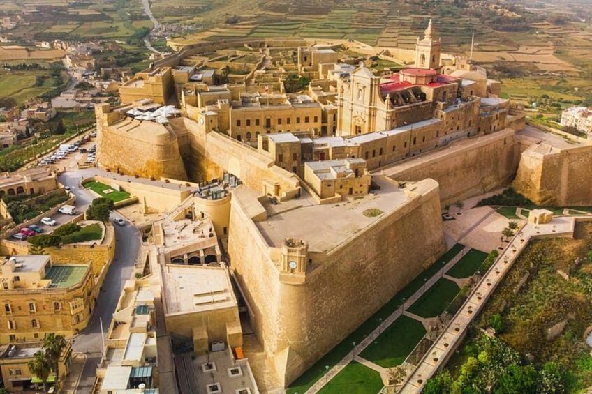 A fortified city with a prominent castle-like structure, a large open square, and surrounding greenery. 5