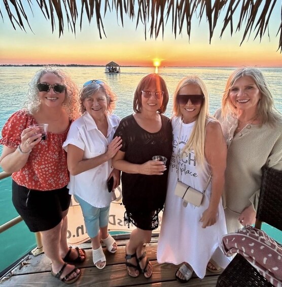A group of people on a boat during sunset with a calm sea and a small boat in the background. 4