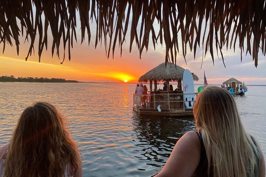 A sunset over water with a boat and a thatched-roof structure. 1