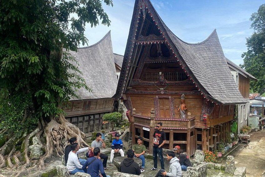 A traditional wooden house with a steeply pitched roof, surrounded by a small garden and a large tree. 4
