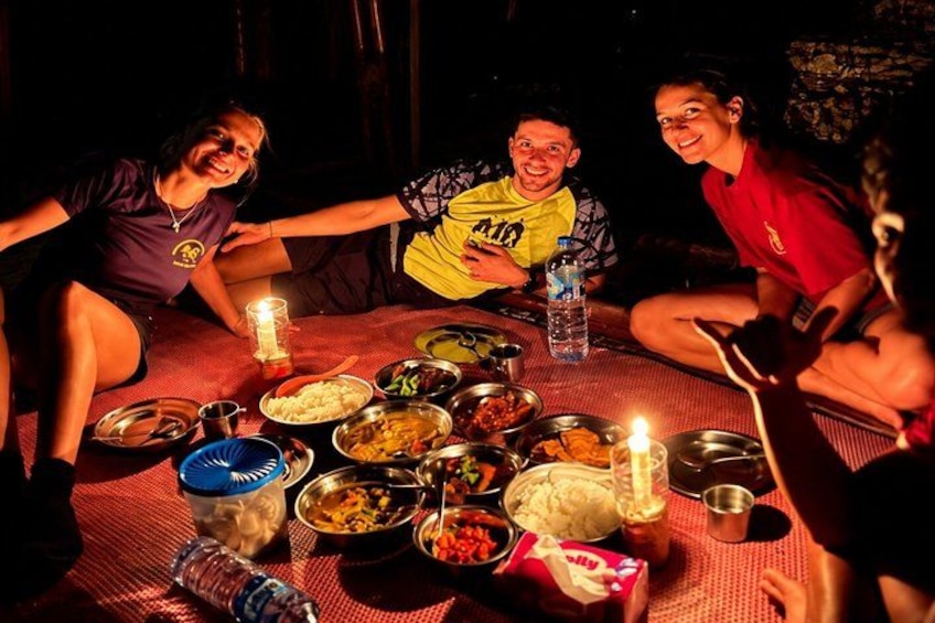 Three people sitting around a table with food and drinks, a candle, and a water bottle. 1