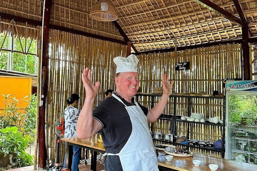 A chef in a bamboo structure with cooking utensils and a display case. 5