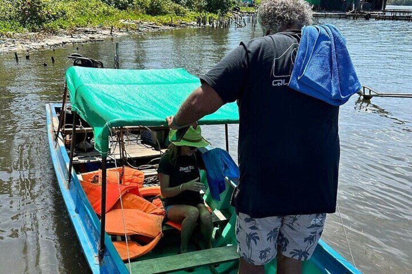 A man in a boat with a green canopy, wearing a black shirt and patterned shorts, and a blue backpack. 5