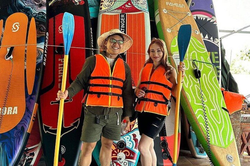 Two people holding paddleboards in front of a row of colorful kayaks. 2