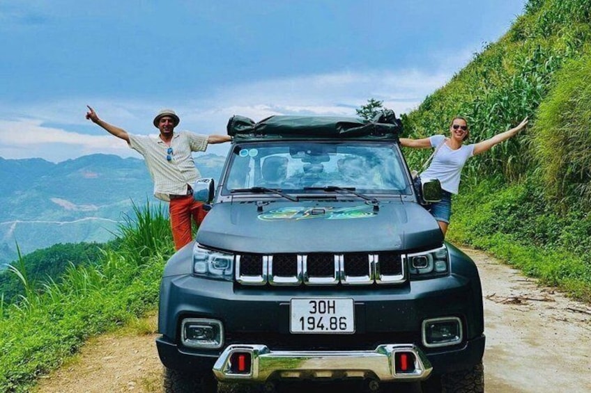 A black SUV parked on a dirt road with two people standing beside it, one on each side. 1