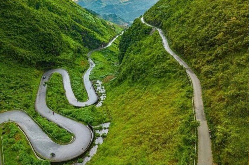 A winding road through a lush green valley with steep hills. 4