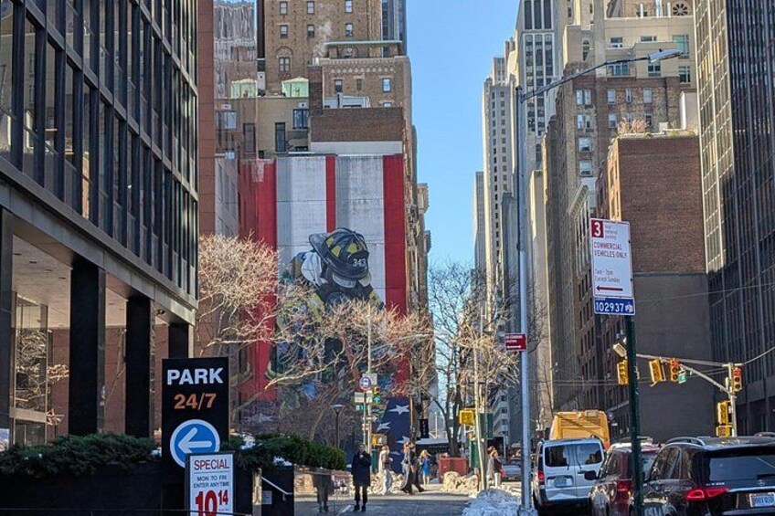 A city street with tall buildings, a fire truck, and a large mural on a building. 3