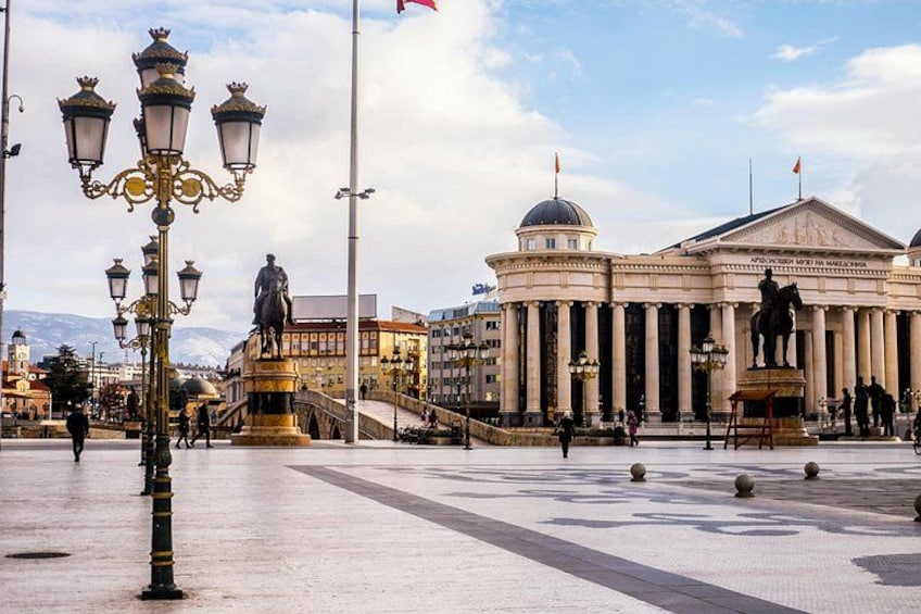 A public square with a statue, a building with columns, and a lamppost. 2