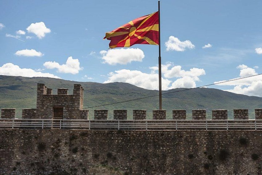 A flag on a flagpole, a stone wall, and a mountainous landscape. 4