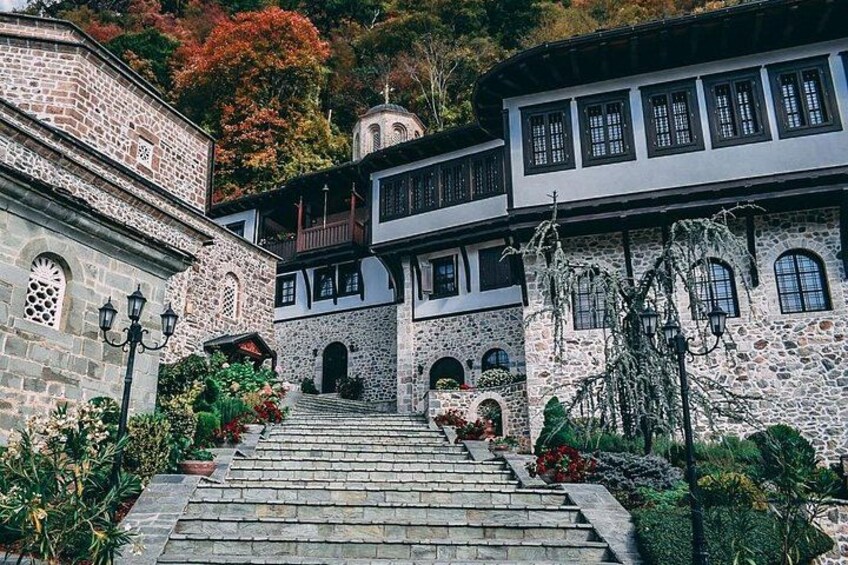 A stone staircase leading to a traditional building with multiple levels, surrounded by lush greenery and autumn-colored trees. 1