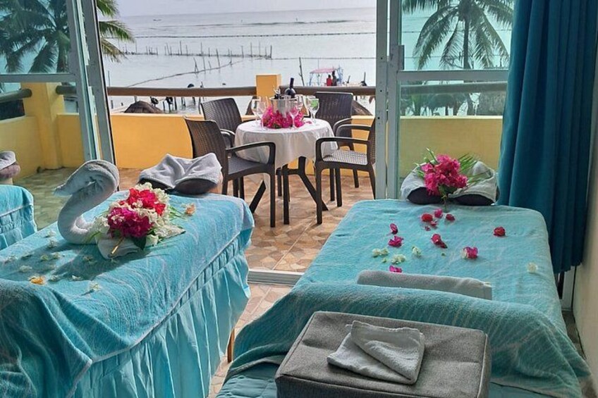 A seaside hotel room with two beds, a dining table, and a view of the ocean. 1