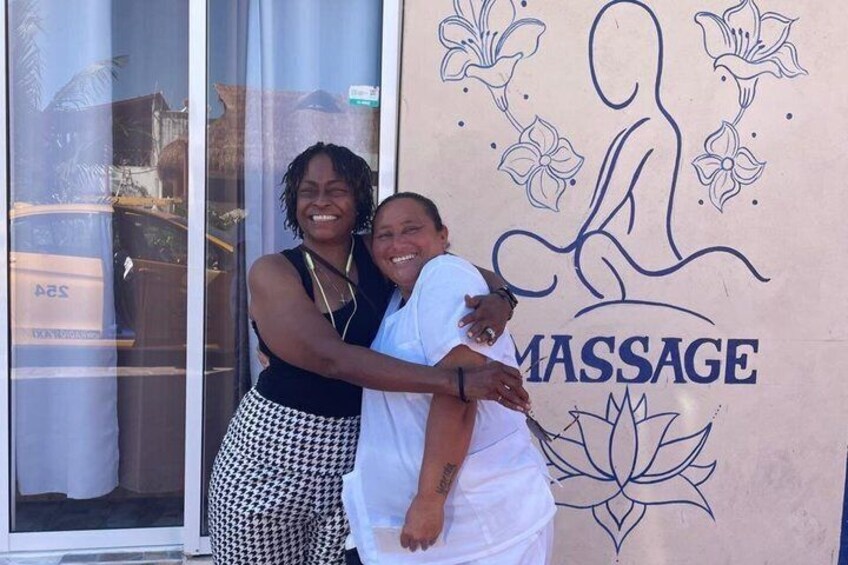 Two people embracing in front of a massage parlor with a lotus flower and stylized human figure logo. 5