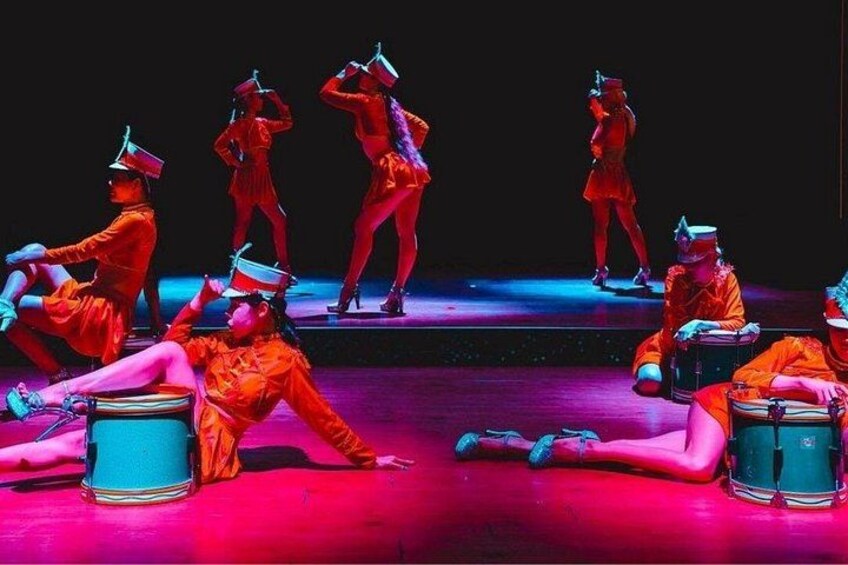 A group of dancers in orange costumes performing on a stage with drums. 5