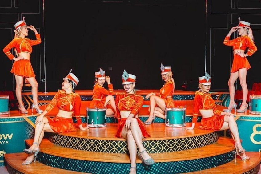 A group of dancers in orange costumes on a stage with a patterned floor and a blue drum. 5