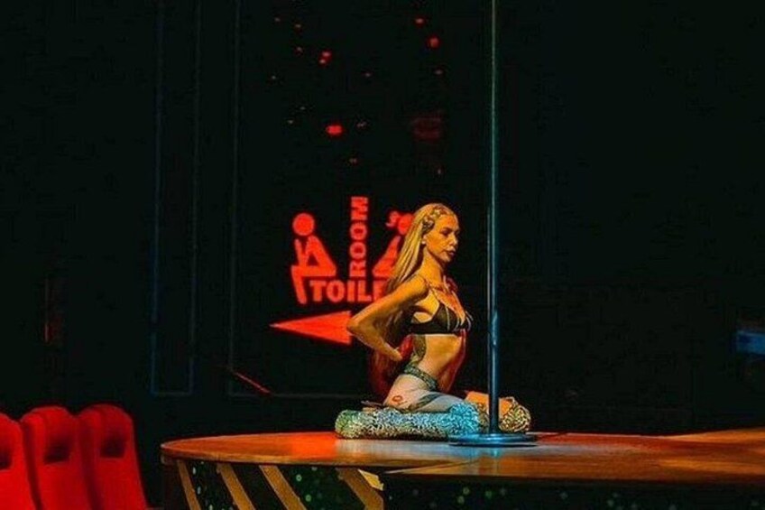 A woman in a bikini on a stage with a sign that says 'TOILET ROOM' in the background. 3