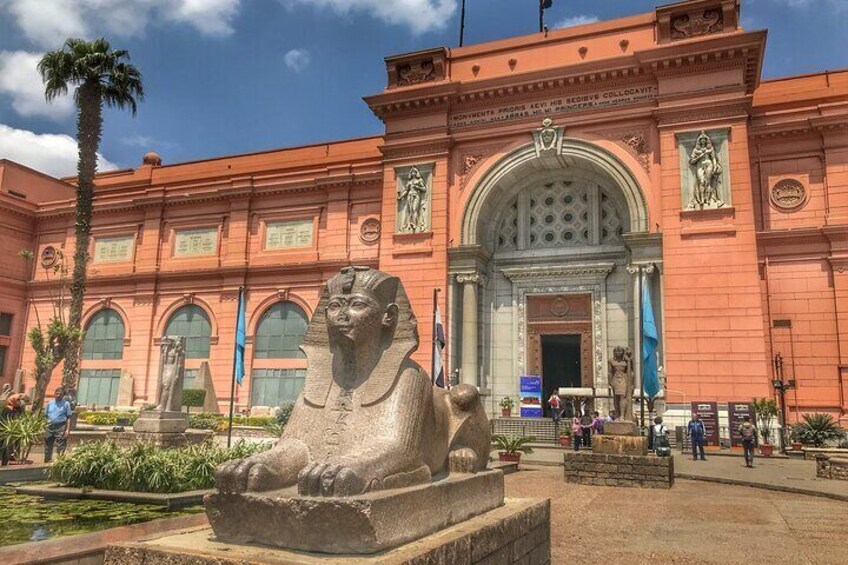 A large sphinx statue in front of a museum with a red facade and arched windows. 2