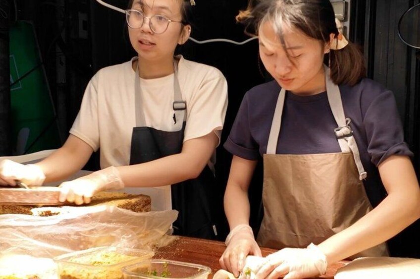 Two individuals preparing food, one wearing a white shirt and the other in a dark shirt, both with aprons. 5