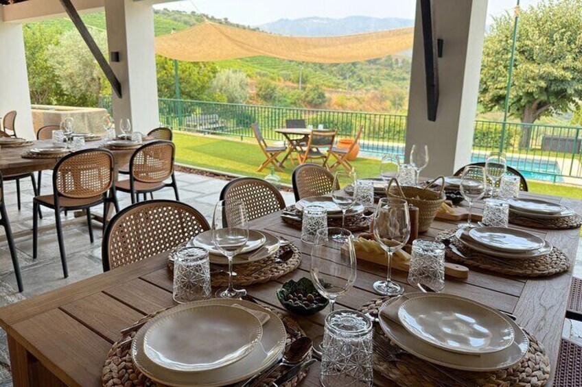 Ein Tisch ist für eine Mahlzeit gedeckt, mit Tellern, Gläsern und einer Karaffe, mit Blick auf eine malerische Landschaft mit Hügeln und einem Zaun. 1