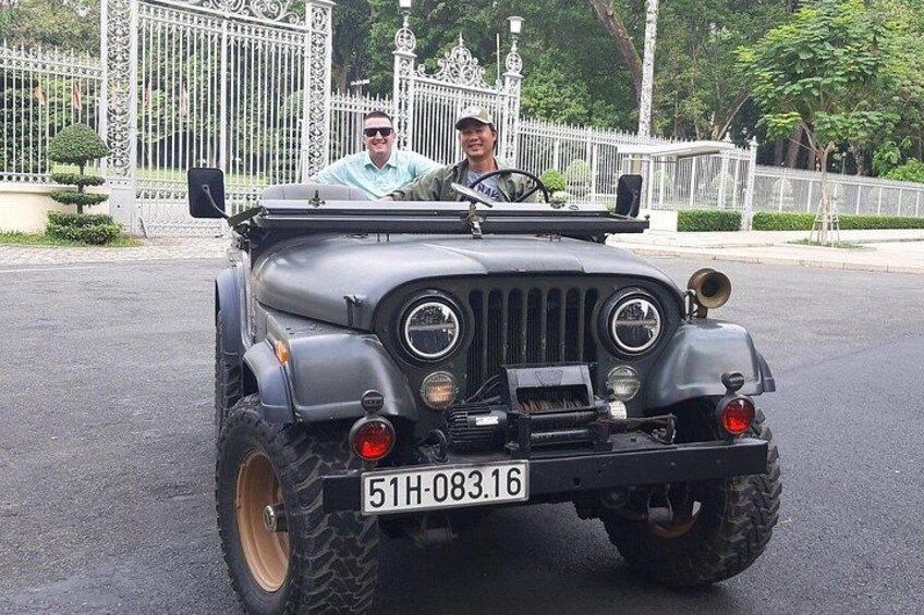 Un'auto militare jeep d'epoca con una targa, parcheggiata di fronte a un cancello bianco decorato. 3