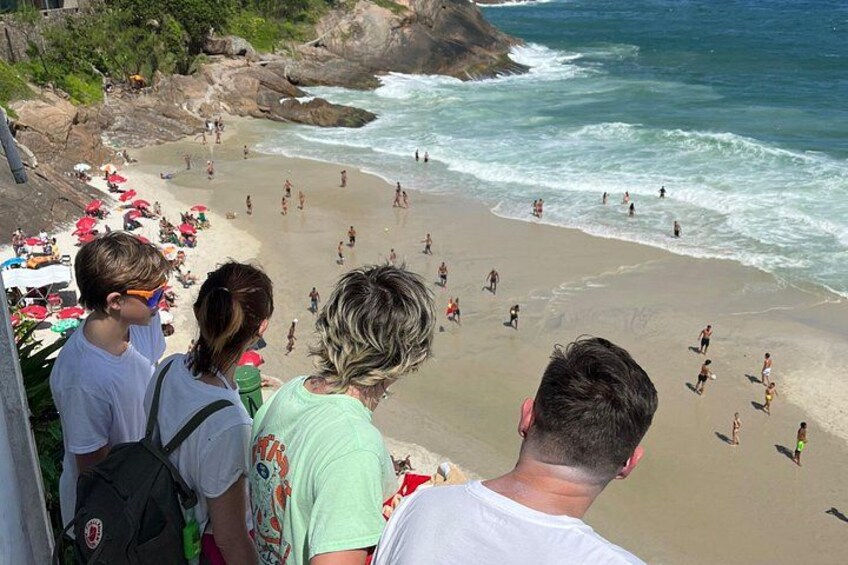 A beach with people swimming and walking, a rocky shoreline, and umbrellas. 5