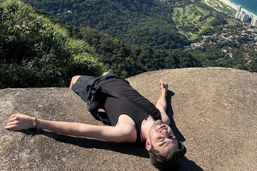 A person lying on a rock with a scenic view of a coastal city and greenery in the background. 4