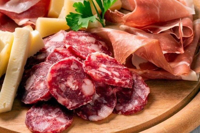 Sliced cured meats, cheese, and a sprig of parsley on a wooden board. 2