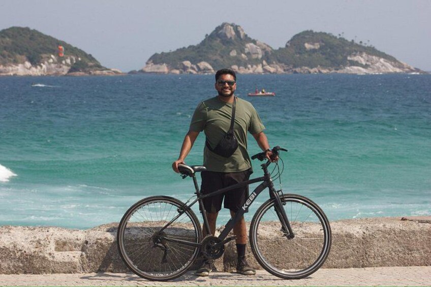 A person standing next to a bicycle by a coastal area with clear blue water and distant islands. 5