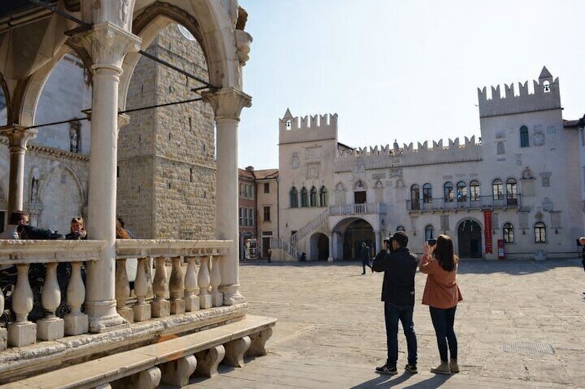 A historic square with a castle in the background, a stone fountain, and people taking photos. 3