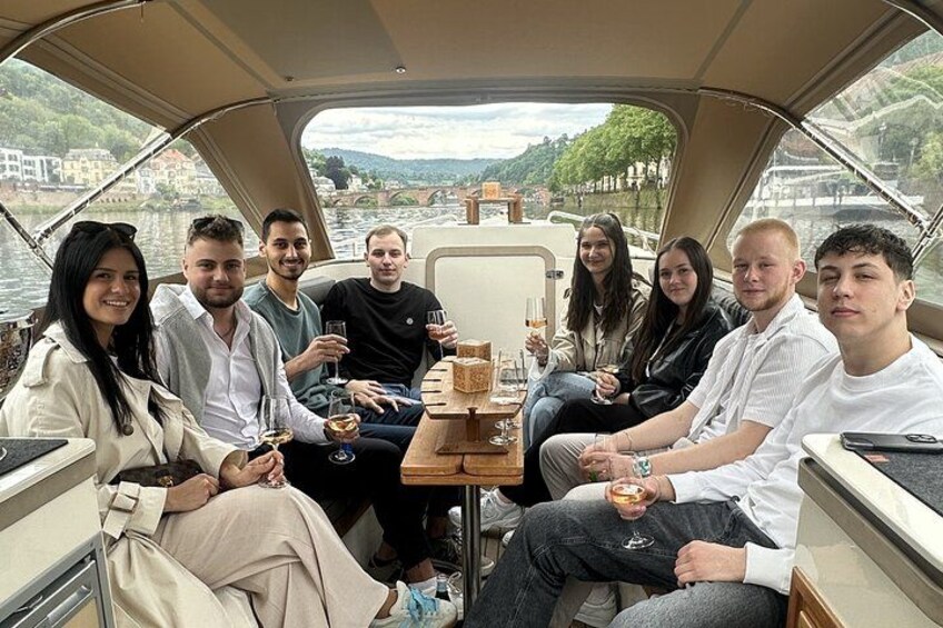 A group of people on a boat with a table in the center, surrounded by water and buildings in the background. 1