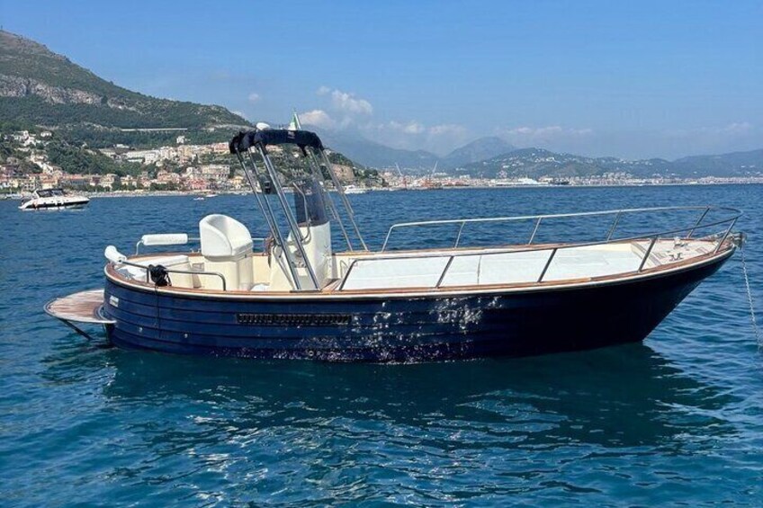 A small motorboat on calm water with a mountainous coastline in the background. 1
