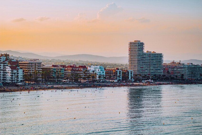 A coastal cityscape with a beach, buildings, and mountains in the background. 5