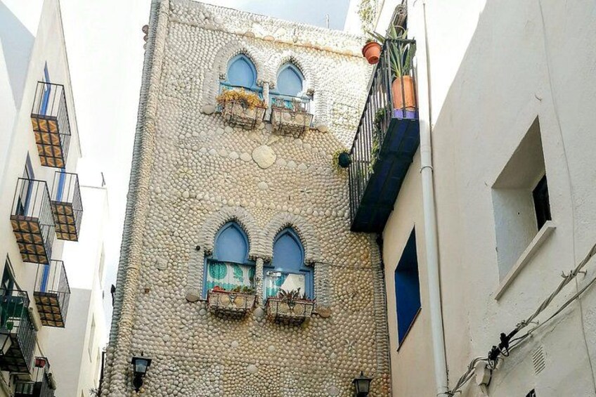 A building with a textured facade, arched windows, and balconies with potted plants. 3