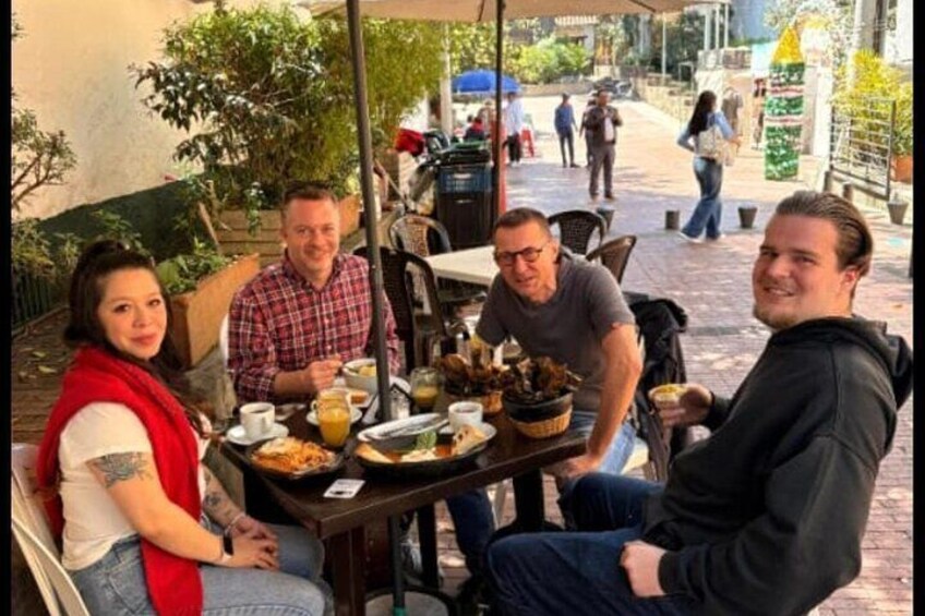 A group of people dining outdoors at a café with tables, chairs, and various dishes. 2