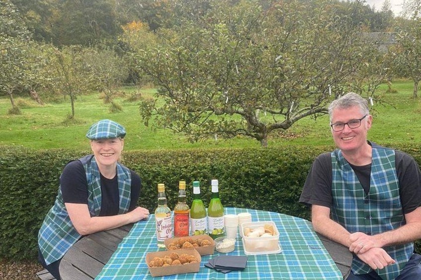 Two people sitting at a table outdoors with food and drinks. 3