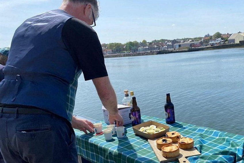A person preparing food on a boat with a tablecloth, bottles, and food items. 4