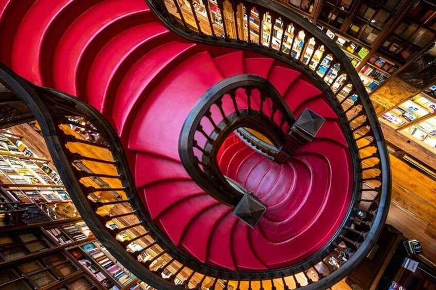 A spiral staircase with red steps and black railings, surrounded by bookshelves. 2
